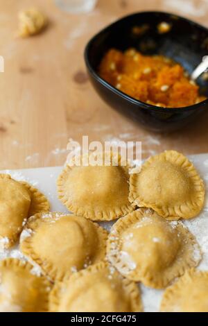 From above of cutting board with neat round raw ravioli on wooden table on background of blurred bottle of olive oil and bowl with pumpkin filling in kitchen Stock Photo
