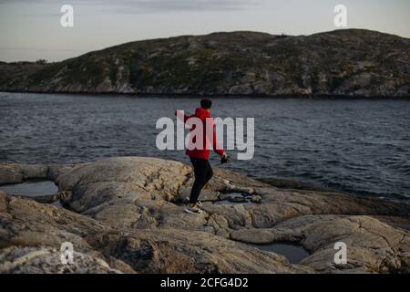 Side view of unrecognizable male traveler in casual wear standing with photo camera on rocky surface near lake and observation tower Stock Photo