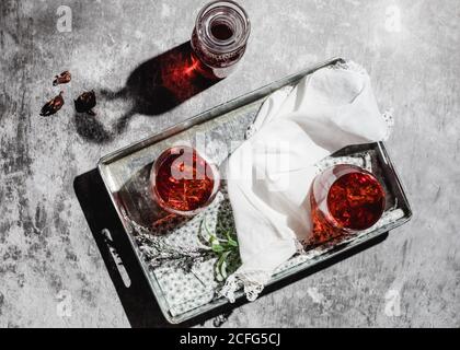 jar and glasses of delicious natural red hibiscus tea placed near pots with dry flowers on table against shabby wall Stock Photo