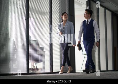 two asian business people on their way to meeting talking while walking in office Stock Photo