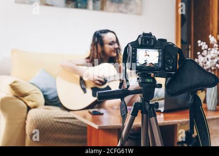 Cute young woman recording an online guitar lesson at home with a camera. Stock Photo