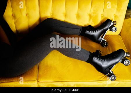 From above of crop unrecognizable black female in roller skates lying on yellow sofa while staying at home during coronavirus lockdown
