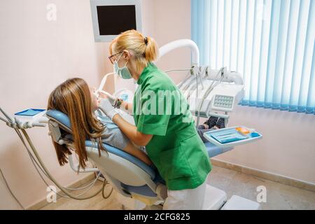 Focused middle aged professional doctor in green uniform examining oral cavity of Woman in dentist chair Stock Photo