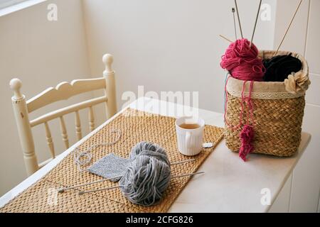Cup of warm tea placed on table near basket with knitting yarn and needles in cozy room Stock Photo