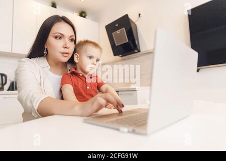 Business mom is using laptop, woman spending time with her boy baby home Stock Photo