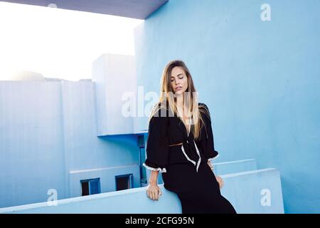 Beautiful Woman leaning on modern blue wall building and looking down Stock Photo