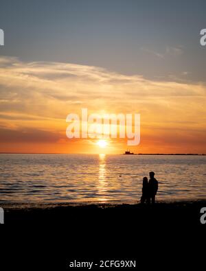 The silhouette of a young couple walking along the Lomma beach while the sun sets behind the nuclear power plant Barsebäck Stock Photo