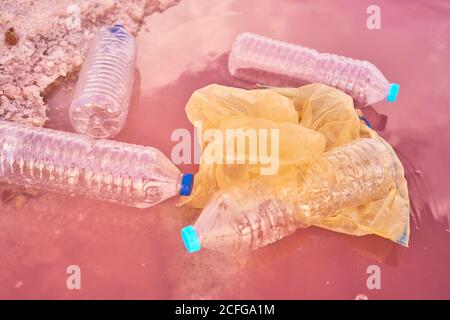Plastic bottles and bags floating near shore at red lagoon with pink salty water Stock Photo