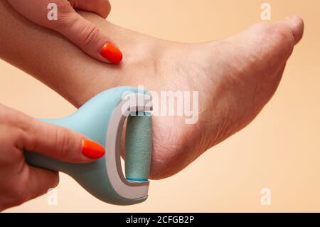 Care and cleansing of the woman feet from rough, flaky skin. An electric foot dead skin remover in a woman's hand grinds foot heel at home Stock Photo
