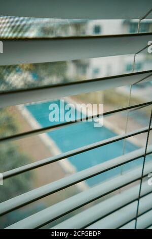 From above view of swimming pool in courtyard through metal jalousie and mosquito net on window Stock Photo