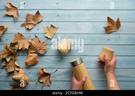 Zero waste eco friendly insulated bamboo flask with bamboo cups. Trendy flat lay with hands holding the flask and natural bamboo cup on aged blue mint Stock Photo