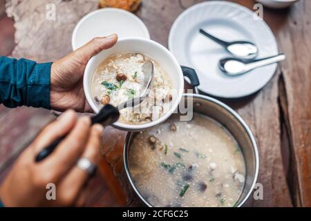 A man scooping rice soup into a bowl. Asian food in the morning. Stock Photo