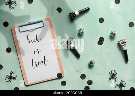 Trick or treat text on clipboard pad on mint green stone background. Flat lay, long shadows of zombie hands. Party decor - paper confetti, party blowe Stock Photo