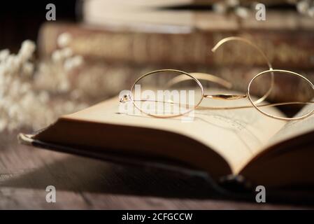 Closeup of opened antique book with old fashioned eyeglasses placed on wooden table Stock Photo