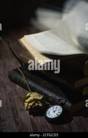 High angle of forgotten stacked books and pocket watch placed on wooden table with dried flower Stock Photo