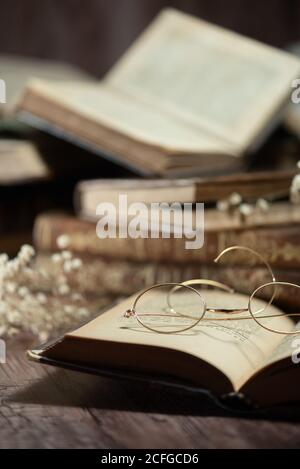 Closeup of opened antique book with old fashioned eyeglasses placed on wooden table Stock Photo