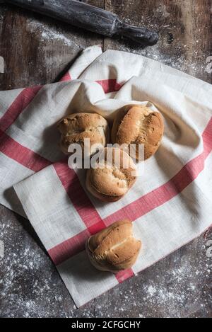 Top view of loaves of fresh bread placed on a kitchen towel on rustic wooden table covered with flour in bakery Stock Photo