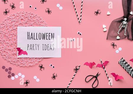 Halloween party ideas text on white page. Flat lay with scissors and Halloween decorations on pink paper background. Top view on hexagon confetti, pap Stock Photo