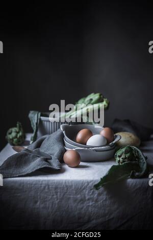 Eggs and different herbs in bowls placed on rustic table Stock Photo
