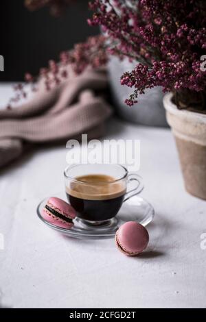 Cup of fresh brewed espresso in glass cup served with pink macaroons on table Stock Photo