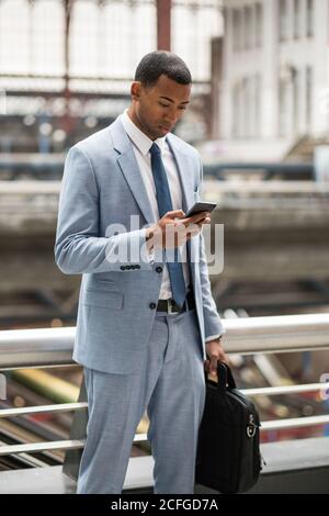 Serious black man in trendy suit using smartphone Stock Photo