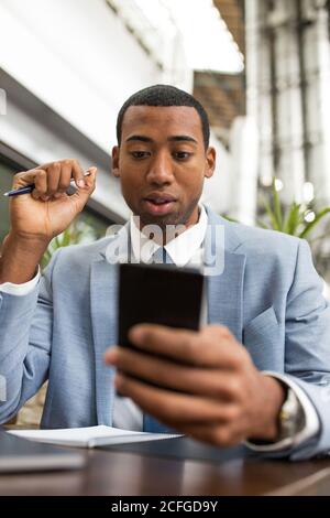 man using smartphone sitting at table with a pen in hand Stock Photo