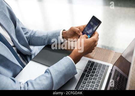 Crop man using laptop and doing calculation on smartphone sitting at table with notepad. Stock Photo