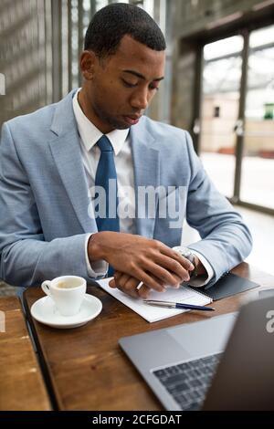 Businessman sitting at desk with cup of freshly brewed coffee and checking watch Stock Photo