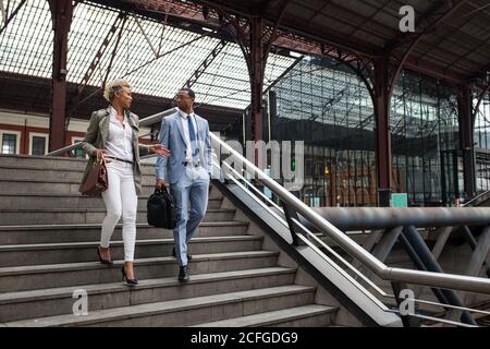 Elegant black Woman and man having talk while walking down stairs on railway station. Stock Photo