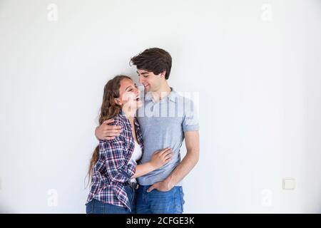 Young couple in casual wear hugging in room with white empty wall Stock Photo