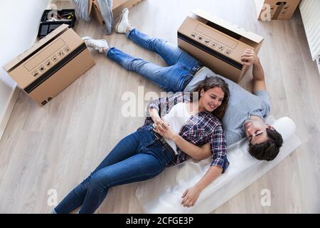 Young couple laying together on floor with carton boxes holding hands and looking at each other Stock Photo