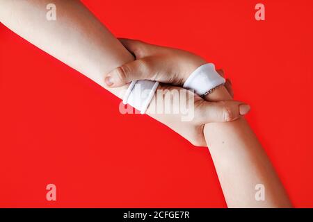 Helping hands concept. Hands with white bracelets on red backgroung. Stock Photo