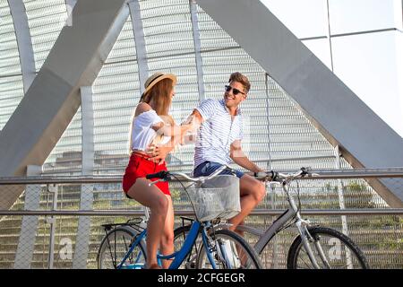 Cute young couple laughing and having fun while riding bicycles in roofed pathway on sunny day Stock Photo