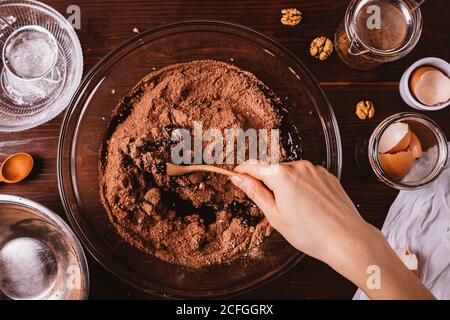 Mixing melted chocolate and cocoa powder in large bowl to make dough for delicious brownie cake on dark wooden table Stock Photo