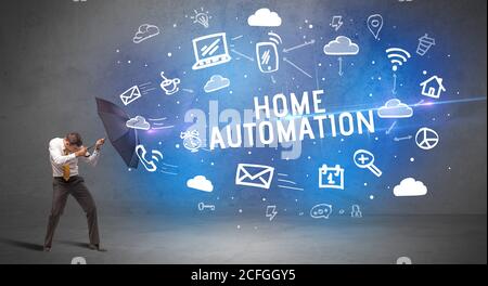 Businessman defending with umbrella from HOME AUTOMATION inscription, modern technology concept Stock Photo