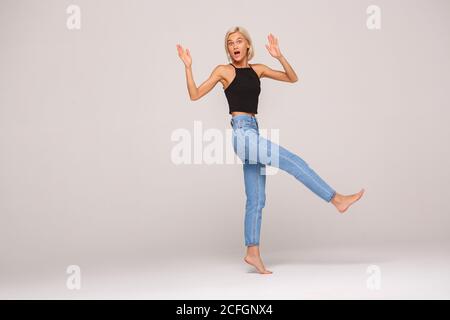 Freestyle. Young blonde woman in jeans and top making step falling down shocked isolated on white full body shot Stock Photo