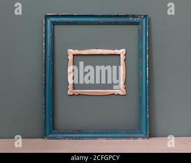 Two empty vintage picture frames, one painted blue, the other a smaller carved frame hanging on a teal colored wall for interior decor Stock Photo