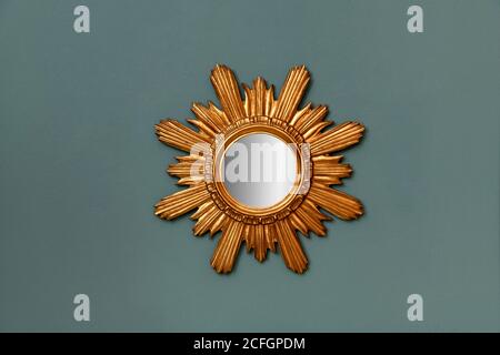 Circular mirror with gilded vintage frame in a star burst pattern hanging on a teal colored wall Stock Photo