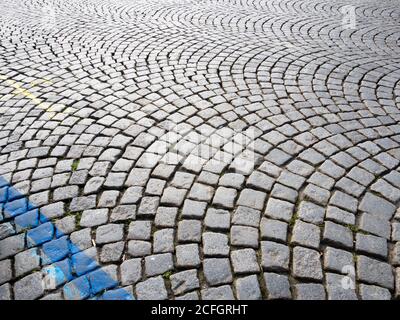 Concentric Cobble Curves: A series of concentric circles form a pattern on a cobbled street in the castle district in Prague. Pavement markings brighten up some stones. Grass sprouts. Stock Photo