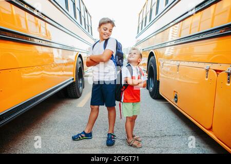 Happy Caucasian brothers students near yellow school bus. Smiling kids going back to school in September. Education system and learning. Support and f Stock Photo