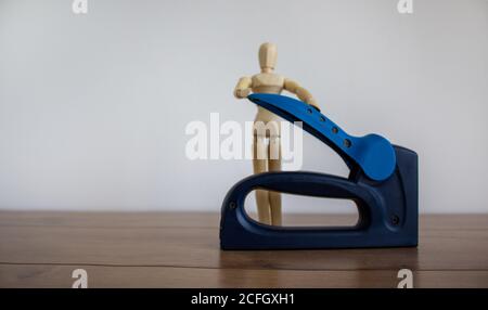 A construction stapler on a wooden table. Wooden model of human. Beautiful white background. Copy space. Stock Photo