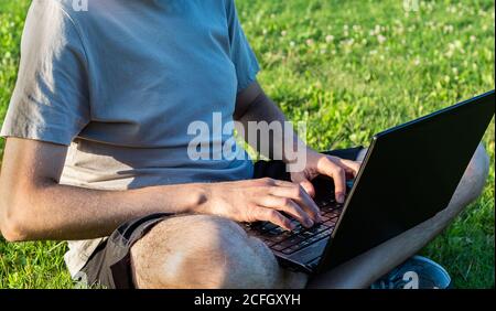 young man sitting on grass and working with laptop Stock Photo