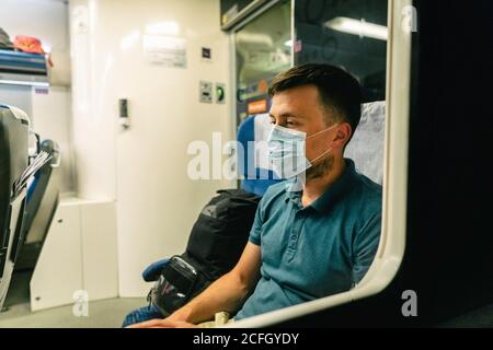 Tired and sad male passenger sits in face shield and looks through the window. View through the window. Topic passenger public transport during Stock Photo