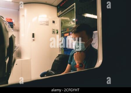 Tired and sad male passenger sits in face shield and looks through the window. View through the window. Topic passenger public transport during Stock Photo