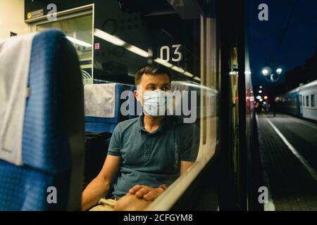 Tired and sad male passenger sits in face shield and looks through the window. View through the window. Topic passenger public transport during Stock Photo