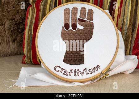 Black embroidered raised power fist on sewing hoop, activism through craft, craftivism text, black lives matter, feminism, senior women joining in pro Stock Photo
