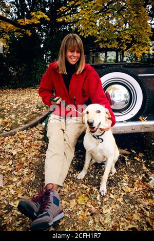 1990s SMILING WOMAN IN RED COAT IN AUTUMN WOODLAND SETTING SITTING ON ANTIQUE CAR BUMPER PETTING YELLOW LABRADOR RETRIEVER DOG - kd6104 WAL004 HARS LAB NOSTALGIC BEAUTY SUBURBAN YELLOW DOMESTIC COLOR RELATIONSHIP SETTING PET CONVERTIBLE OLD TIME NOSTALGIA OLD FASHION AUTO 1 JUVENILE STYLE VEHICLE SECURITY YOUNG ADULT PEACE TEAMWORK PLEASED JOY LIFESTYLE FEMALES RURAL GROWNUP HEALTHINESS TRANSPORT COPY SPACE FULL-LENGTH LADIES PERSONS AUTOMOBILE CARING LABRADOR SERENITY CONFIDENCE TRANSPORTATION EYE CONTACT FREEDOM HAPPINESS MAMMALS WELLNESS CHEERFUL LEISURE STRENGTH AUTOS CANINES HUMANS Stock Photo