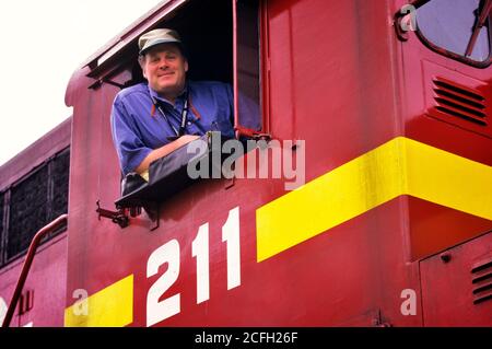 1990s PORTRAIT OF TRAIN ENGINEER LEANING OUT OF TRAIN CAB WINDOW SMILING LOOKING AT CAMERA - kr115094 DEG002 HARS VEHICLE ENGINE ENGINEER RAILROAD LIFESTYLE CAB JOBS GROWNUP HORIZONTAL TRANSPORT COPY SPACE PERSONS GROWN-UP MALES CONFIDENCE TRANSPORTATION MIDDLE-AGED FREIGHT WINDOWS MIDDLE-AGED MAN EYE CONTACT RELEASES RAIL SKILL OCCUPATION HAPPINESS SKILLS HEAD AND SHOULDERS LOW ANGLE POWERFUL LABOR PRIDE AUTHORITY EMPLOYMENT LOCOMOTIVE OCCUPATIONS DIESEL MOBILITY VEHICLES RAILROADS EMPLOYEE COOPERATION DIESEL LOCOMOTIVE CAUCASIAN ETHNICITY LABORING OLD FASHIONED Stock Photo