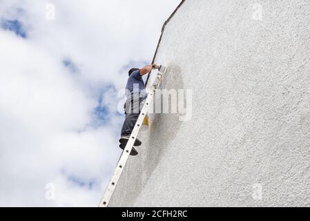Man up a high ladder painting gable end of pebbledash house. Stock Photo