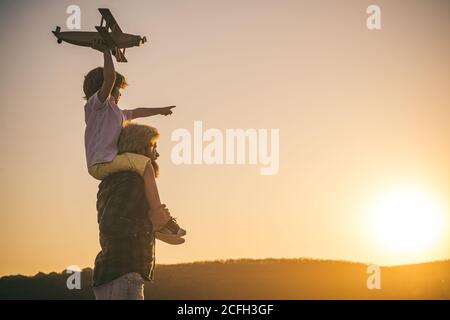 Happy child. Sunset silhouette of Father and son together. Boy child is sitting on daddy shoulder piggyback while the flight. Stock Photo